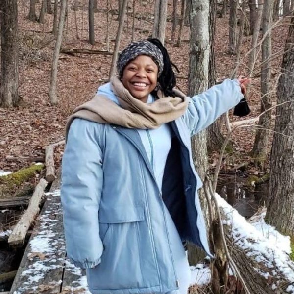 Lisa standing on a snowy bridge in the forest, smiling at the camera