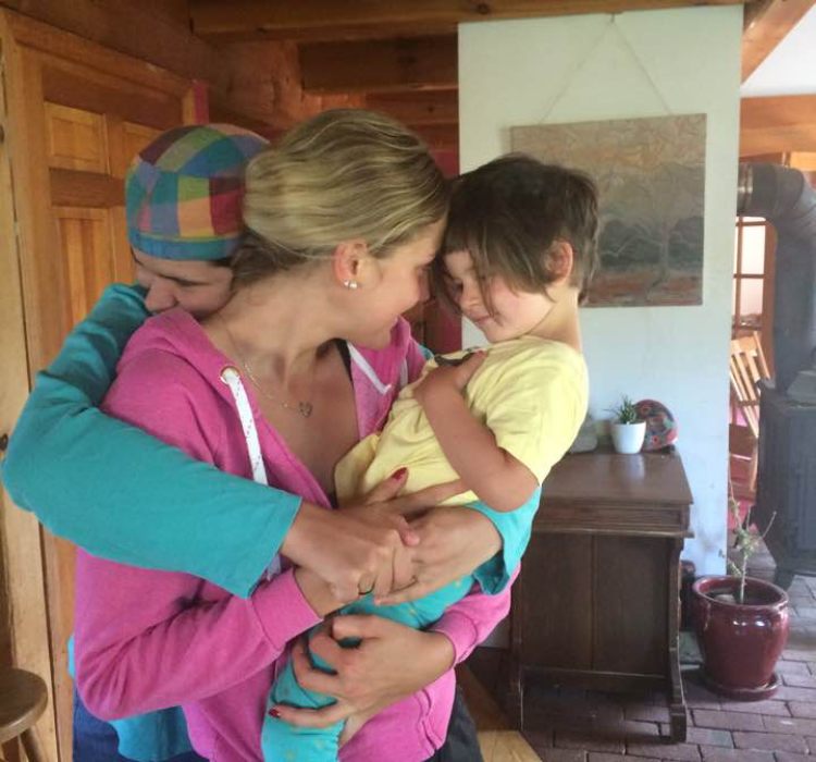 Anna holding a toddler while they smile at each other. A second adult hugs the two of them.