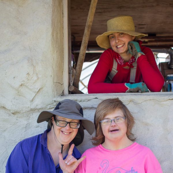 Hannah smiling through a window with two Camphill residents smiling below the window