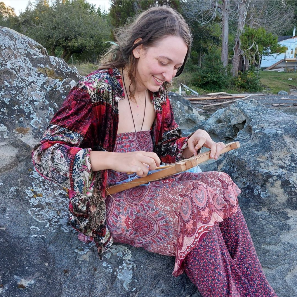 Zoe sitting on a large rock and smiling while doing a craft