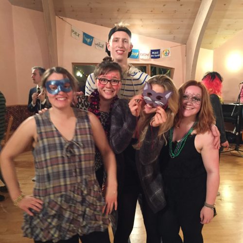 Five smiling people wearing mardi gras masks and necklaces