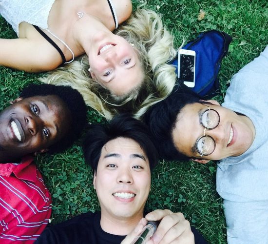 Anna and three friends lying in grass, their heads all together in a circle, looking up