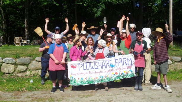 A crowd of people smiling and holding a banner that reads Plowshare Farm Living, Working, and Diversifying the Greenfield Community since 1990