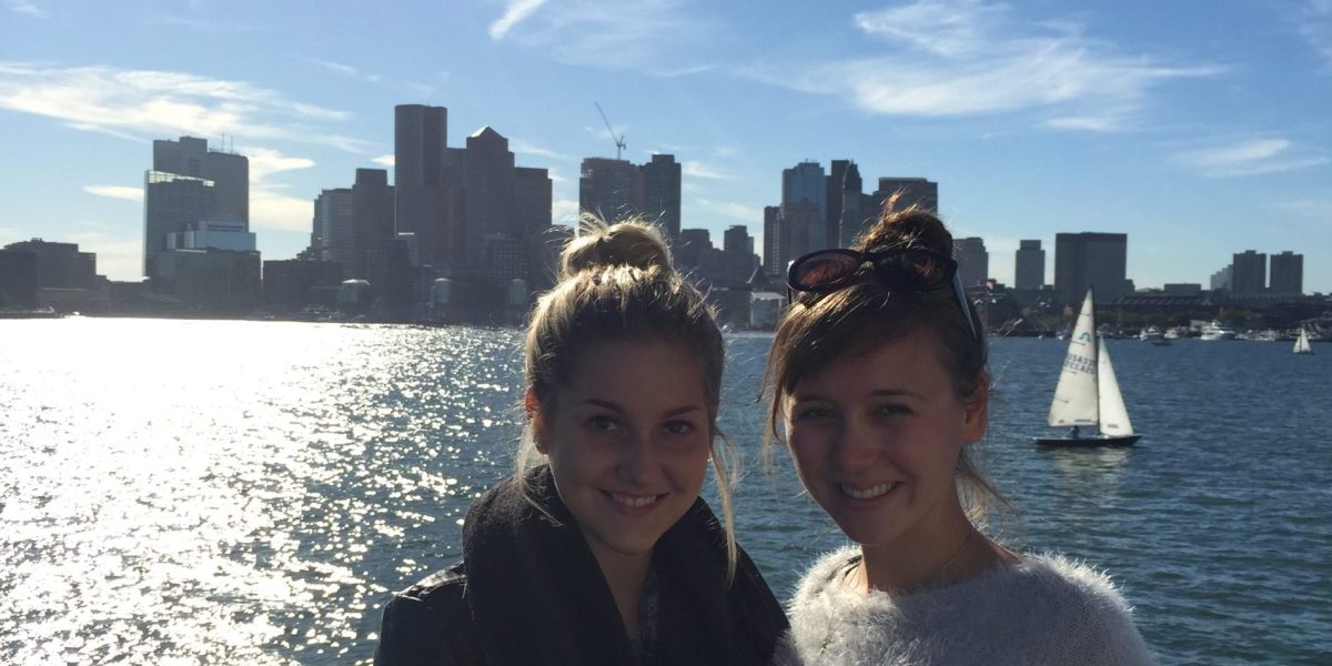 Anna and friend smiling at the camera with the Boston skyline in the background