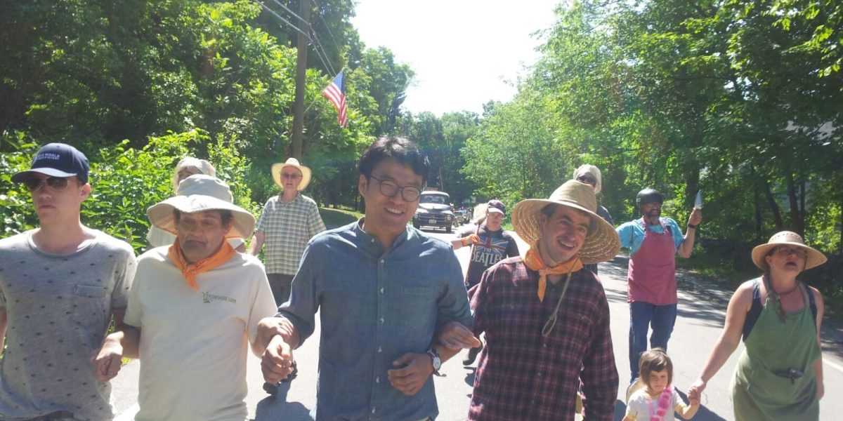 A row of Camphill residents and volunteers walking down a tree-lined street. They are all holding hands and smiling.