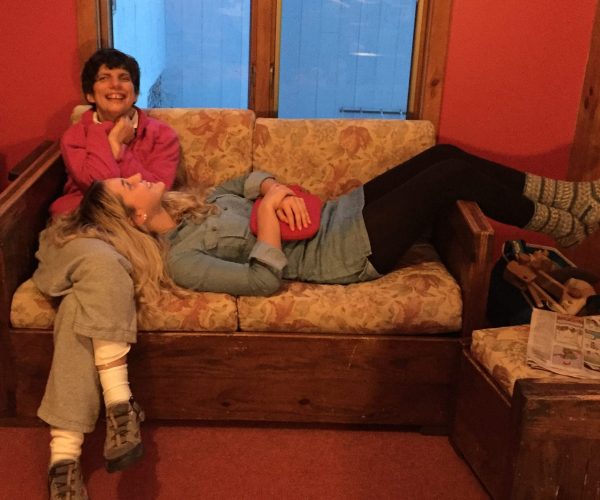 Anna lays on a couch with her head in the lap of an adult woman Camphill resident. They are both smiling.