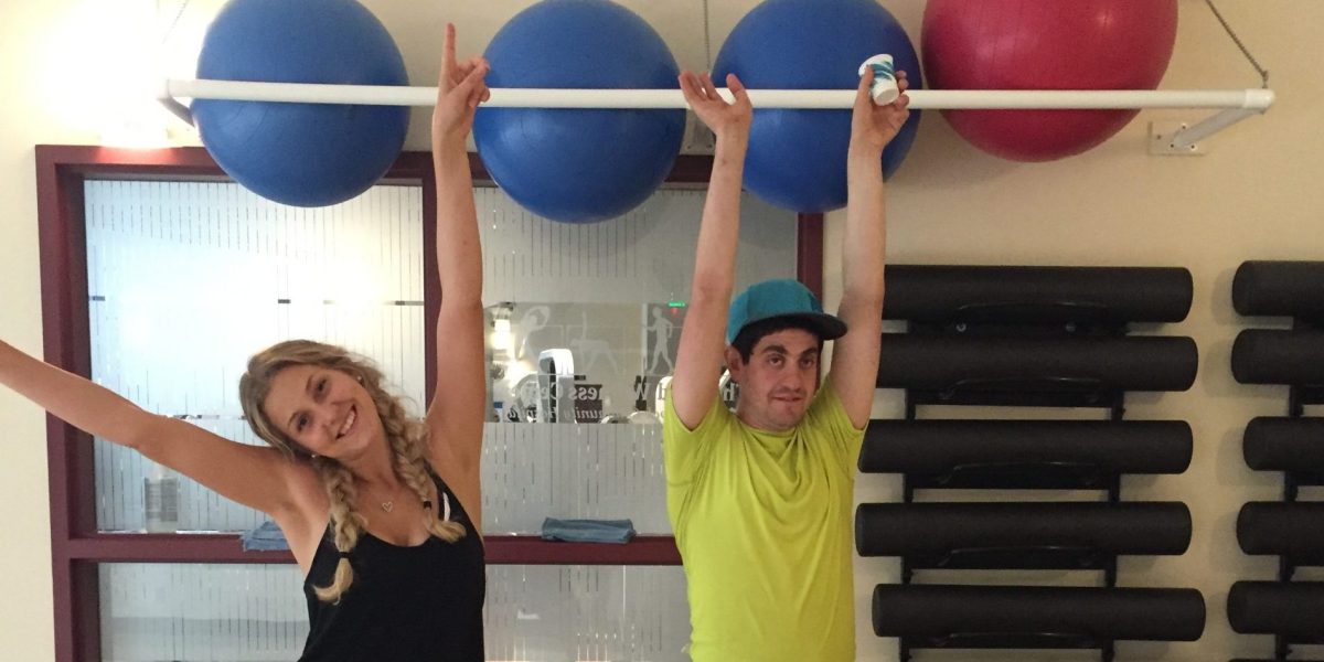 Anna and a Camphill resident smiling with their arms held in the air. Behind them are exercise balls.