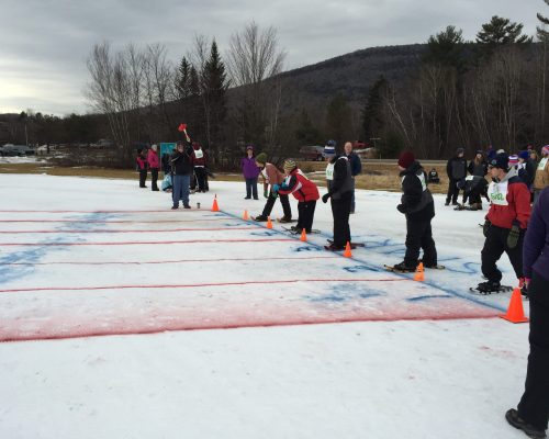 Crowd of people in snowshoes line up to walk across painted lines in the snow.