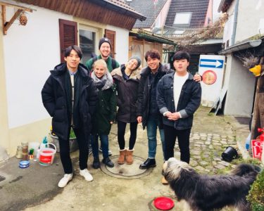 Six people standing together and smiling at the camera with a dog in the foreground, looking at them