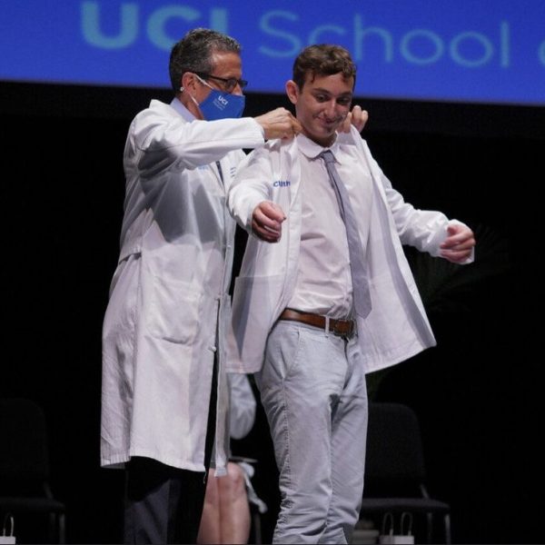 Nicolo smiles while a doctor helps him put his white coat on at his white coat ceremony.