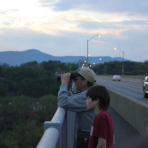 Two people, one young and one older stand next to each other admiring the view off the Rip Van Winkle Bridge. The older man (Elias) has binoculars.