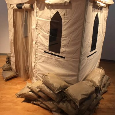 A canvas military style confession booth equipped with sand bags, and mosquito nets